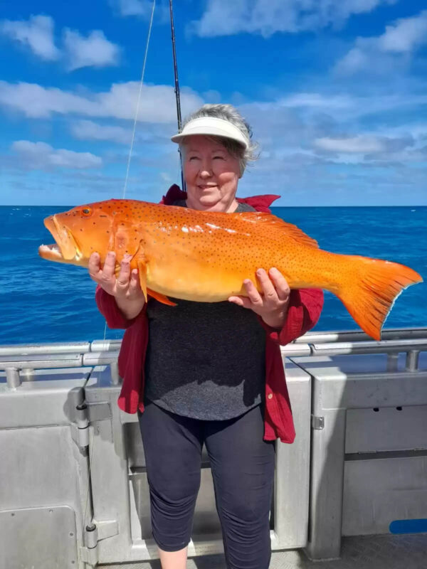Woman in red jacket holding a red emperor fish she just caught